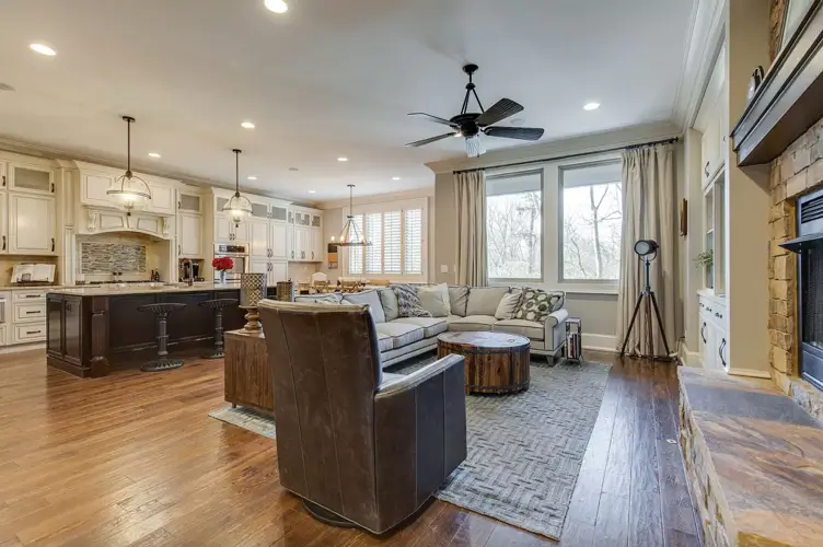 A large, open-concept modern farmhouse interior featuring white kitchen cabinets, a dark wood island, a stone fireplace, dark wood floors, and a light gray L-shaped sectional sofa.