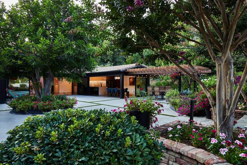 Modern outdoor patio with pergola, lush landscaping, and dining area surrounded by trees