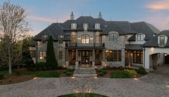 Dave Ramsey house in Franklin Tennessee showing French Country stone and stucco exterior with steeply pitched slate roof and manicured landscaping