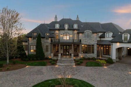 Dave Ramsey house in Franklin Tennessee showing French Country stone and stucco exterior with steeply pitched slate roof and manicured landscaping