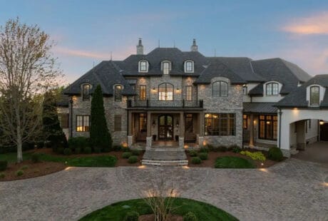 Dave Ramsey house in Franklin Tennessee showing French Country stone and stucco exterior with steeply pitched slate roof and manicured landscaping