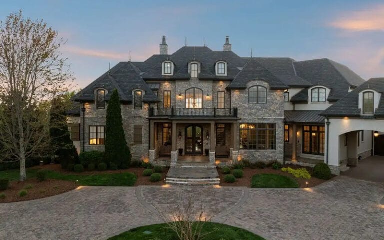 Dave Ramsey house in Franklin Tennessee showing French Country stone and stucco exterior with steeply pitched slate roof and manicured landscaping