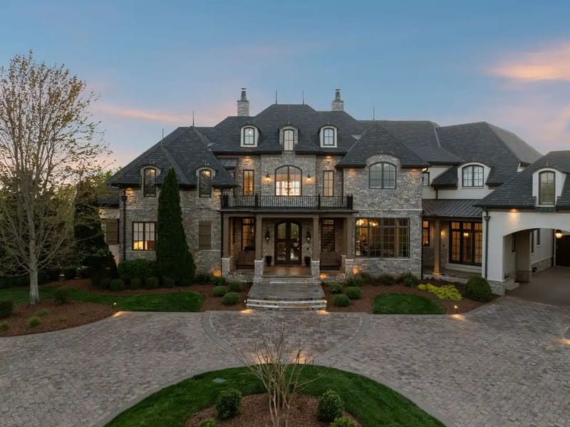 Dave Ramsey house in Franklin Tennessee showing French Country stone and stucco exterior with steeply pitched slate roof and manicured landscaping