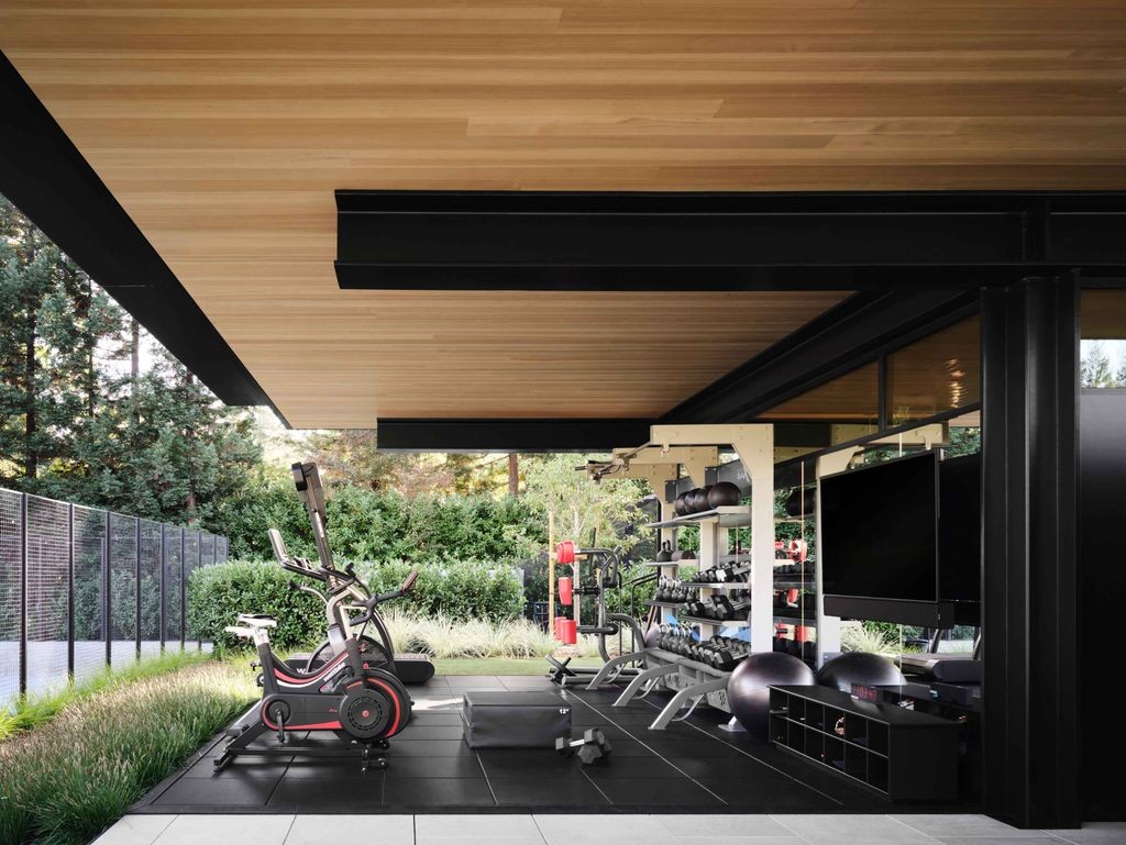 Modern luxury home gym with sleek fitness equipment, mirrored walls, and large windows overlooking greenery