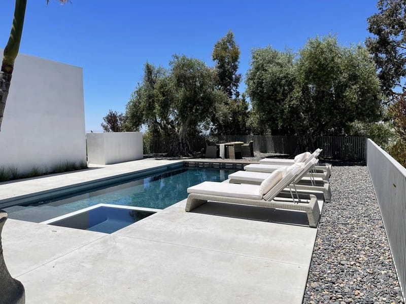 Modern rectangular swimming pool with lounge chairs and minimalist white walls at Jay Shetty house