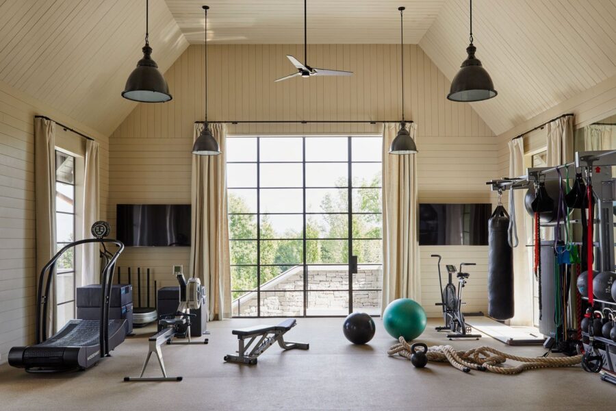 Spacious luxury home gym with high ceilings, large windows, treadmill, power rack, and punching bag in natural light