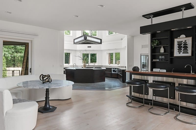 The chef's kitchen and bar area in Bobby Bones' Nashville house featuring a sleek black island, built-in bar with stools, marble-topped surfaces, and large windows flooding the space with natural light