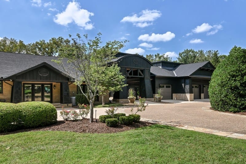 The exterior of Bobby Bones' Nashville house showcasing modern dark-toned architecture with a curved roof, large windows, and a multi-car garage under a bright blue sky