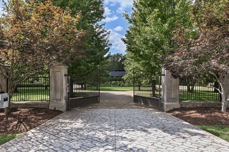 The gated entrance to Bobby Bones' Nashville estate on Franklin Pike, featuring ornate black iron gates, stone pillars, and a manicured driveway lined with mature trees