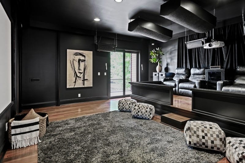 The home theater in Bobby Bones' Nashville house with black leather recliners, checkered ottomans, a projector setup, and ceiling-mounted speakers