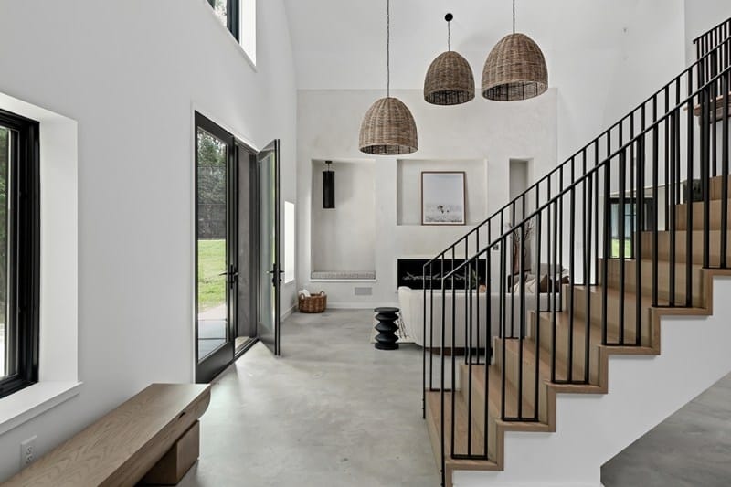The interior of Bobby Bones' Nashville house with polished concrete floors, black-framed glass doors, woven pendant lights, a modern fireplace, and minimalist decor