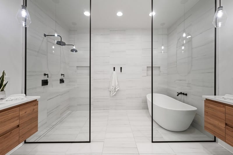 The master bathroom in Bobby Bones' Nashville house with a freestanding tub, glass-enclosed shower, dual wooden vanities, marble tile, and black fixtures