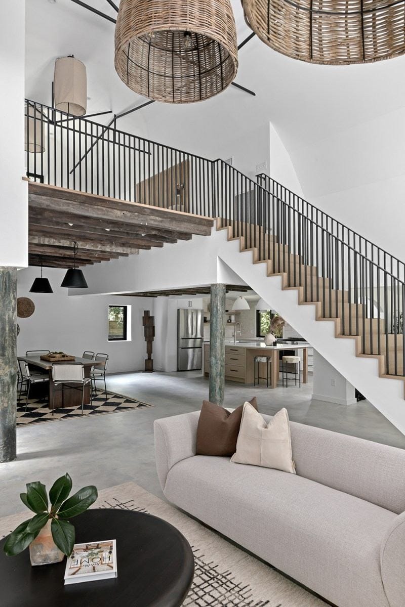 The open-concept living and dining area in Bobby Bones' Nashville house featuring wicker pendant lights, a two-story staircase with black metal railings, and a seamless flow into the kitchen
