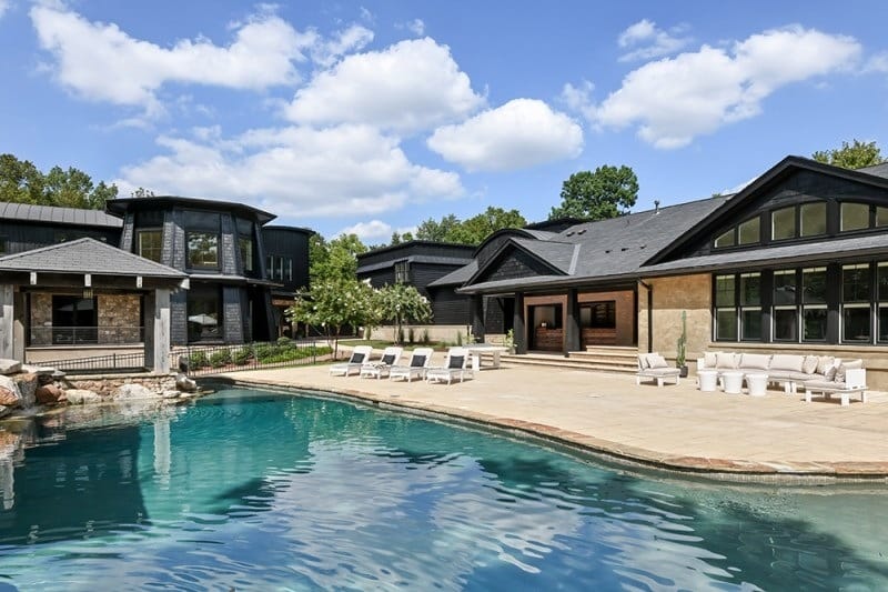 The resort-style swimming pool and stone-accented patio at Bobby Bones' Nashville estate with the contemporary guest house featuring angular architecture and expansive windows