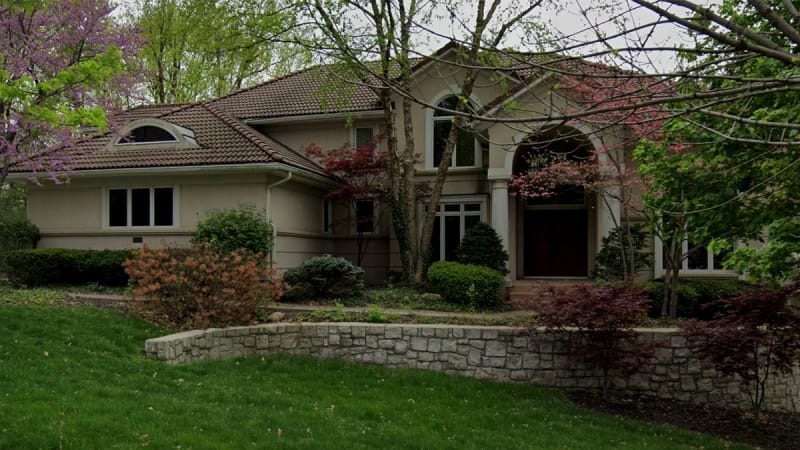 Two-story house with brown tiled roof, beige exterior, and arched entryway in Kansas City's Briarcliff West neighborhood