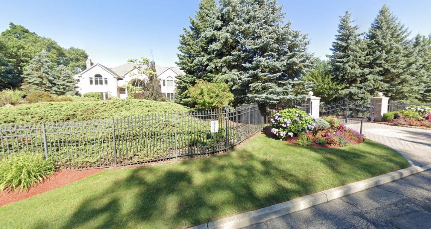 Street-facing view of Chris Rock's Alpine estate with wrought-iron gate, landscaping and mature trees
